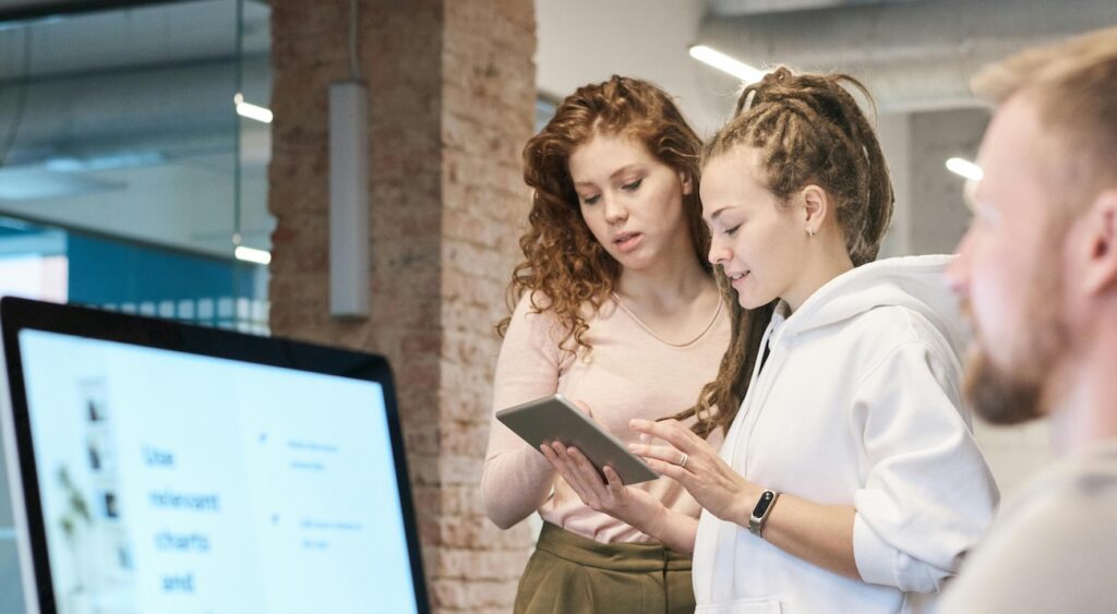 Photo Of Man Near Computer with 2 Women Stading Beside Photo Of Man Near Computer with 2 Women Stading Beside