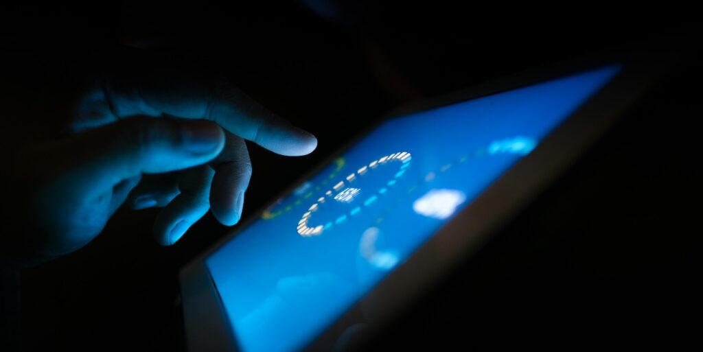 Close-up of a hand interacting with a glowing touchscreen in a dark setting Close-up of a hand interacting with a glowing touchscreen in a dark setting