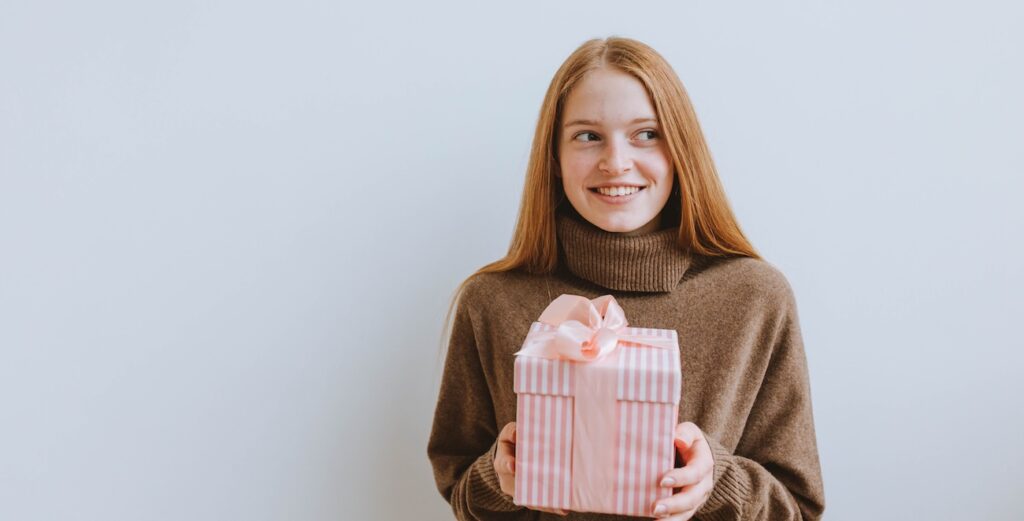 A cheerful woman in a cozy sweater holding a pink gift box