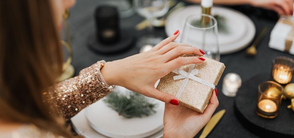 A woman holding a glittery gift at a festive dinner table A woman holding a glittery gift at a festive dinner table