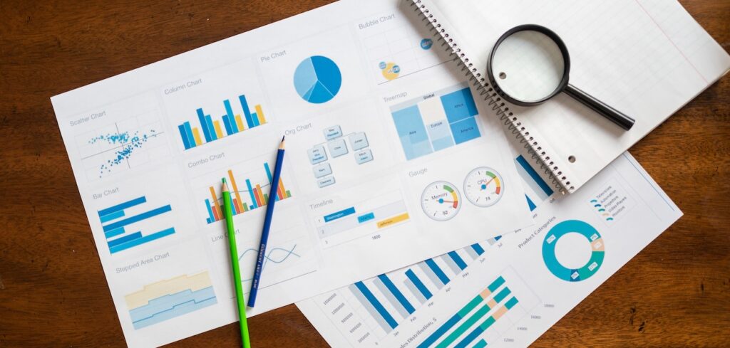 view of financial charts, magnifying glass, and stationery on wooden table